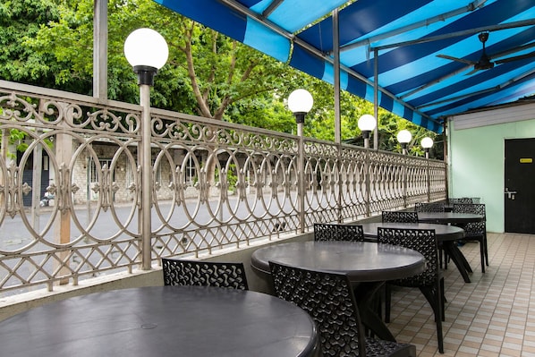 An outdoor café with round tables and chairs, a decorative metal fence, and a blue awning. - Hotel Platinum (Mumbai)