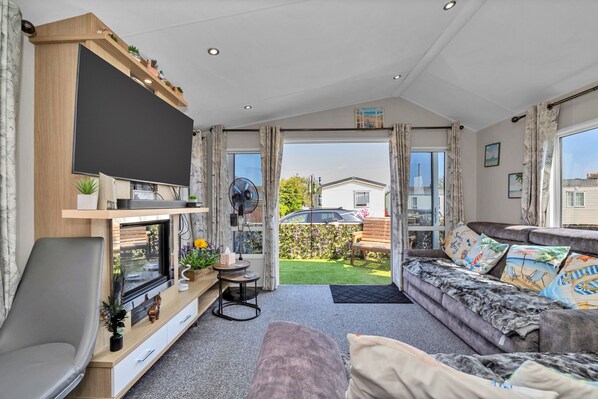 A modern living room with a flat-screen TV, a sofa, a dining table, and a view of the backyard.