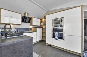 A modern kitchen with white cabinetry, a built-in oven, and a stainless steel microwave.