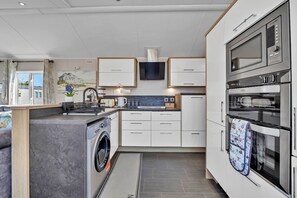 A compact kitchen with a washing machine, microwave, oven, and a flat-screen TV.