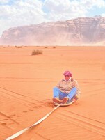 Una persona sentada en un trineo en un desierto, con una montaña rocosa al fondo.