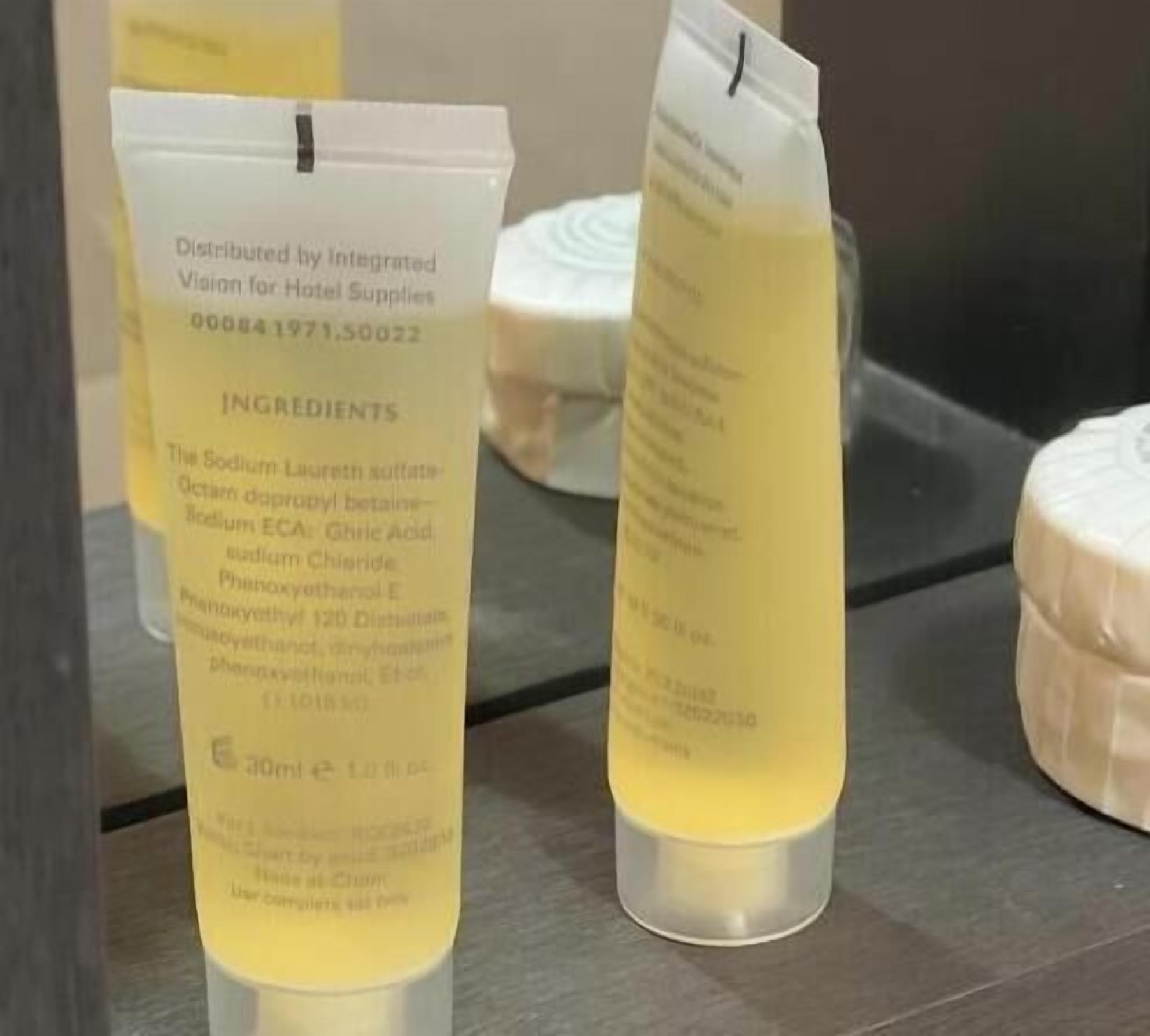 Two tubes of a skincare product with visible ingredients and a label indicating it is distributed by Integrated Vision for Hotel Supplies.
