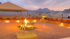 An outdoor seating area with tables and chairs, a fire pit, and a view of mountains. - Horizon Star Golden Camp (Wadi Rum)