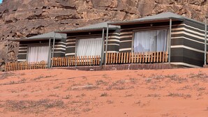 A desert landscape with a large rock formation in the background and a row of striped-roofed cabins in the foreground. - Horizon Star Golden Camp (Wadi Rum)