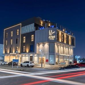 Un edificio moderno con un letrero que dice 'Lounge', múltiples ventanas y un estacionamiento con coches.