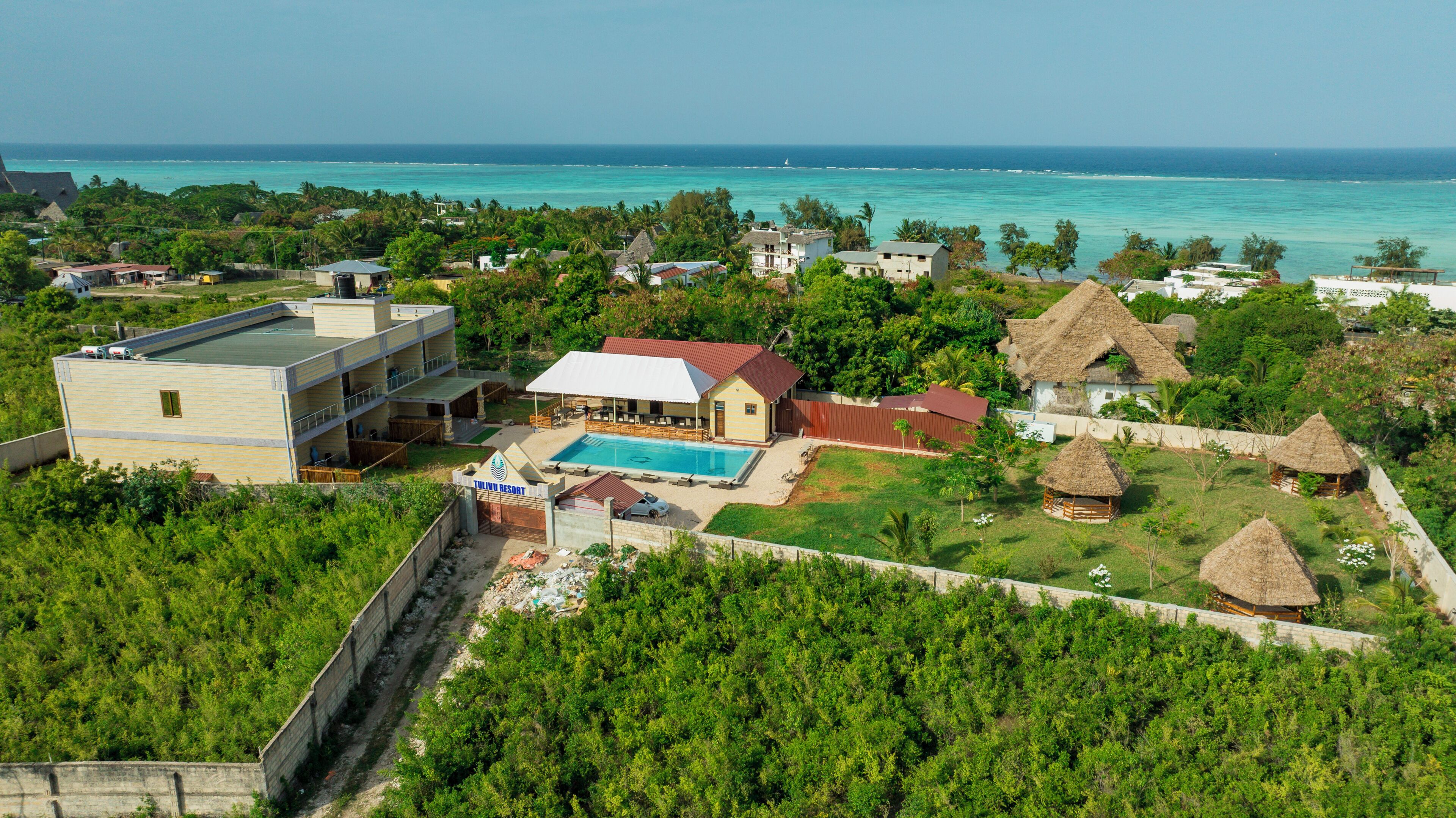 A resort with a swimming pool, thatched-roof structures, and a view of the ocean.
