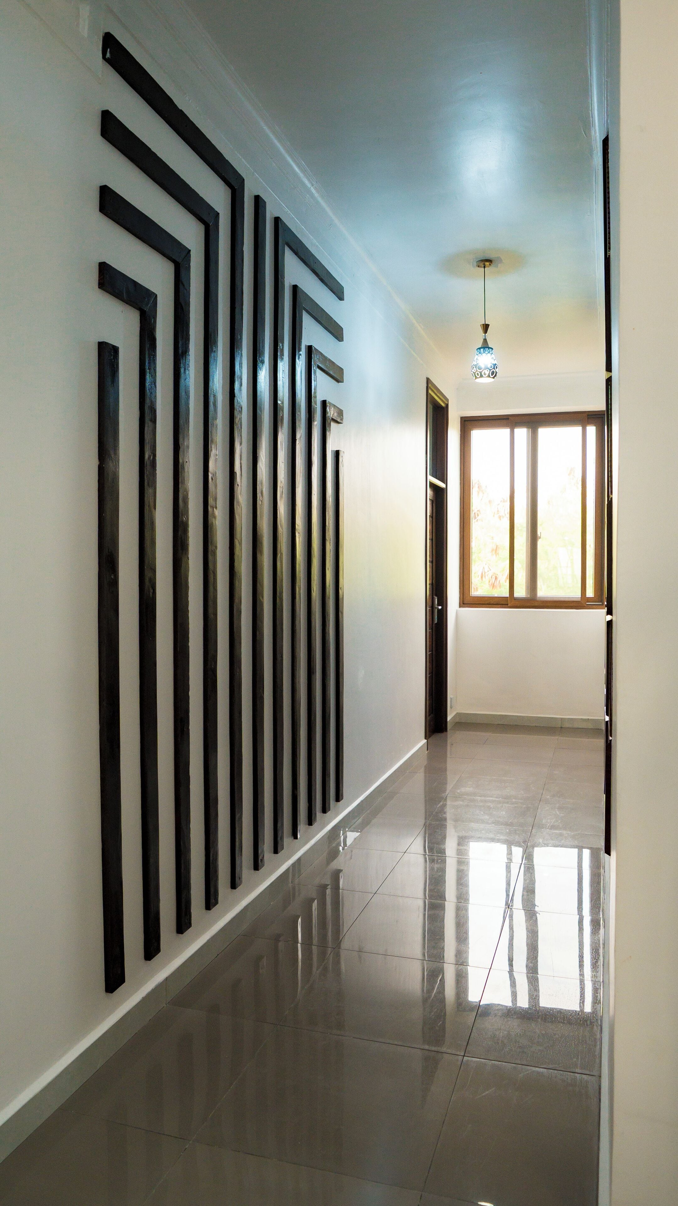 A hallway with a polished floor, a light fixture, and a door leading to a room with a window.