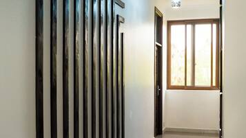 A hallway with a polished floor, a light fixture, and a door leading to a room with a window.