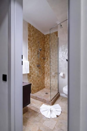 Une douche avec une porte en verre, un mur carrelé et une serviette blanche sur le sol.