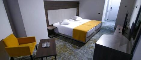 A hotel room with a bed, a yellow chair, a small table, and a TV.