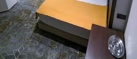 A hotel room with a bed, a bedside table, a nightstand, a wall-mounted air conditioner, and a door.