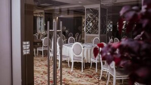 A dining area with round tables, white chairs, and a patterned carpet.