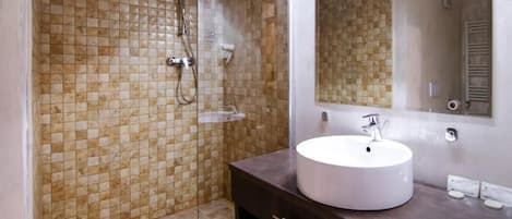 Un baño con pared de ducha azulejada, un lavabo blanco y un espejo grande.