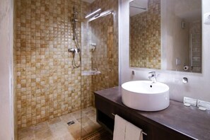 A bathroom with a tiled shower wall, a white sink, and a large mirror.