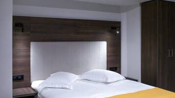 A modern hotel room with a large bed, a wooden headboard, and a wardrobe.