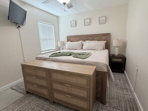 A bedroom with a bed, bedside lamps, a TV mounted on the wall, and a wooden dresser. - Waterfront Condo - Walk To Beach - Heated Pool (Treasure Island)