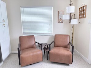 A room with two leather chairs, a small table, a window with blinds, a wall-mounted lamp, and a framed picture. - Waterfront Condo - Walk To Beach - Heated Pool (Treasure Island)