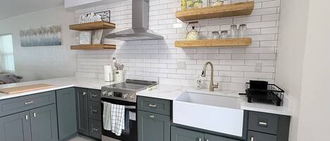 A modern kitchen with grey cabinets, a stainless steel stove, a white sink, and wooden shelves above the counter.