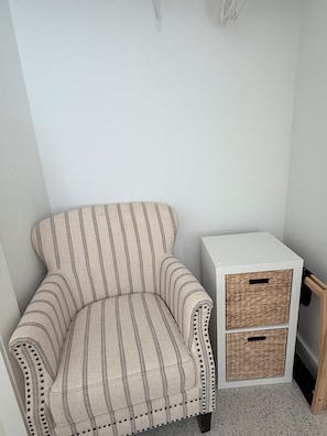 Ein Eckzimmer mit einem gestreiften Sessel, einem weißen Beistelltisch mit Korbwannen und einem Holzschrank.