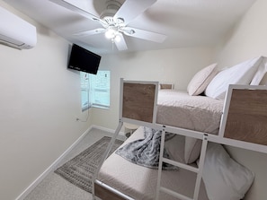 Ein Schlafzimmer mit Etagenbett, Deckenventilator, Fernseher, Fenster mit Jalousien und Teppich.