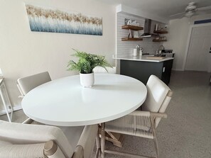 A dining area with a round white table, four chairs, a potted plant, and a kitchen in the background. - Waterfront Condo - Walk To Beach - Heated Pool (Treasure Island)
