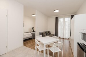 Ein kompakter Wohnbereich mit Küchenzeile, einem Essbereich mit weißem Tisch und Stühlen, einer Couch und einem Bett.