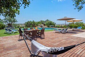 Eine Holzterrasse mit Pool, Liegestühlen und Sonnenschirmen.