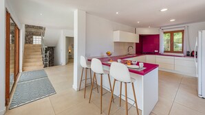 Een moderne keuken met een centraal eiland, barstoelen, een inbouwoven en een raam met gordijnen.