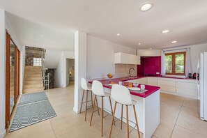 A modern kitchen with a central island, bar stools, a built-in oven, and a window with curtains. - SON JERONIO (Muro)