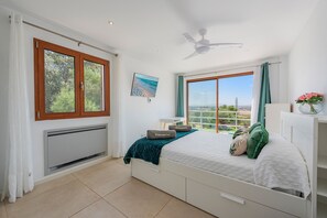 A bedroom with a bed, a ceiling fan, a window with curtains, a radiator, and a view of the outdoors. - SON JERONIO (Muro)