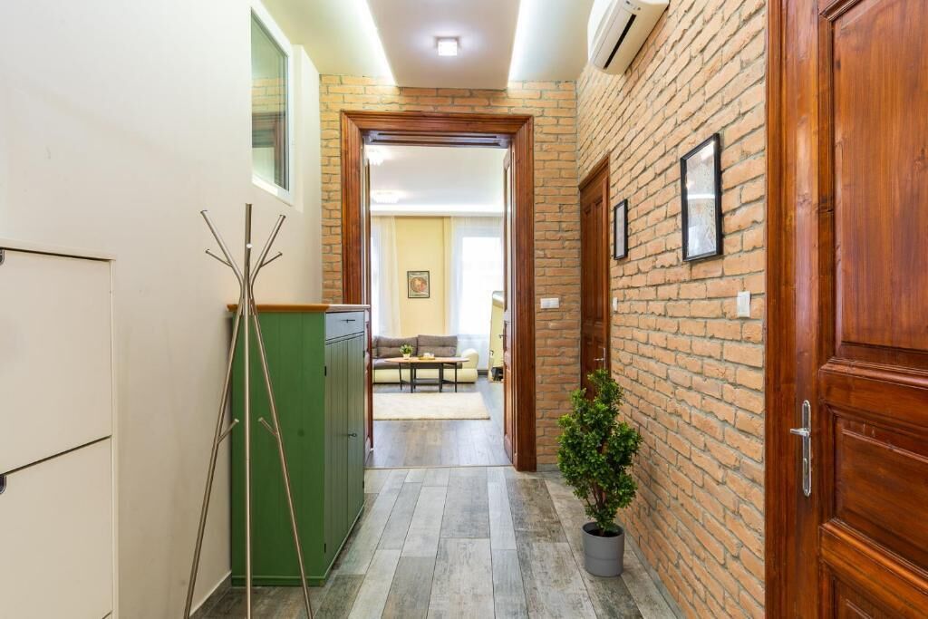 Un passadís amb una paret de maó, una porta de fusta, un armari verd i una planta en test.