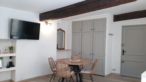 Ein Essbereich mit einem runden Tisch, vier Korbstühlen, einem Flachbildfernseher an der Wand und einem Holzbalken an der Decke.