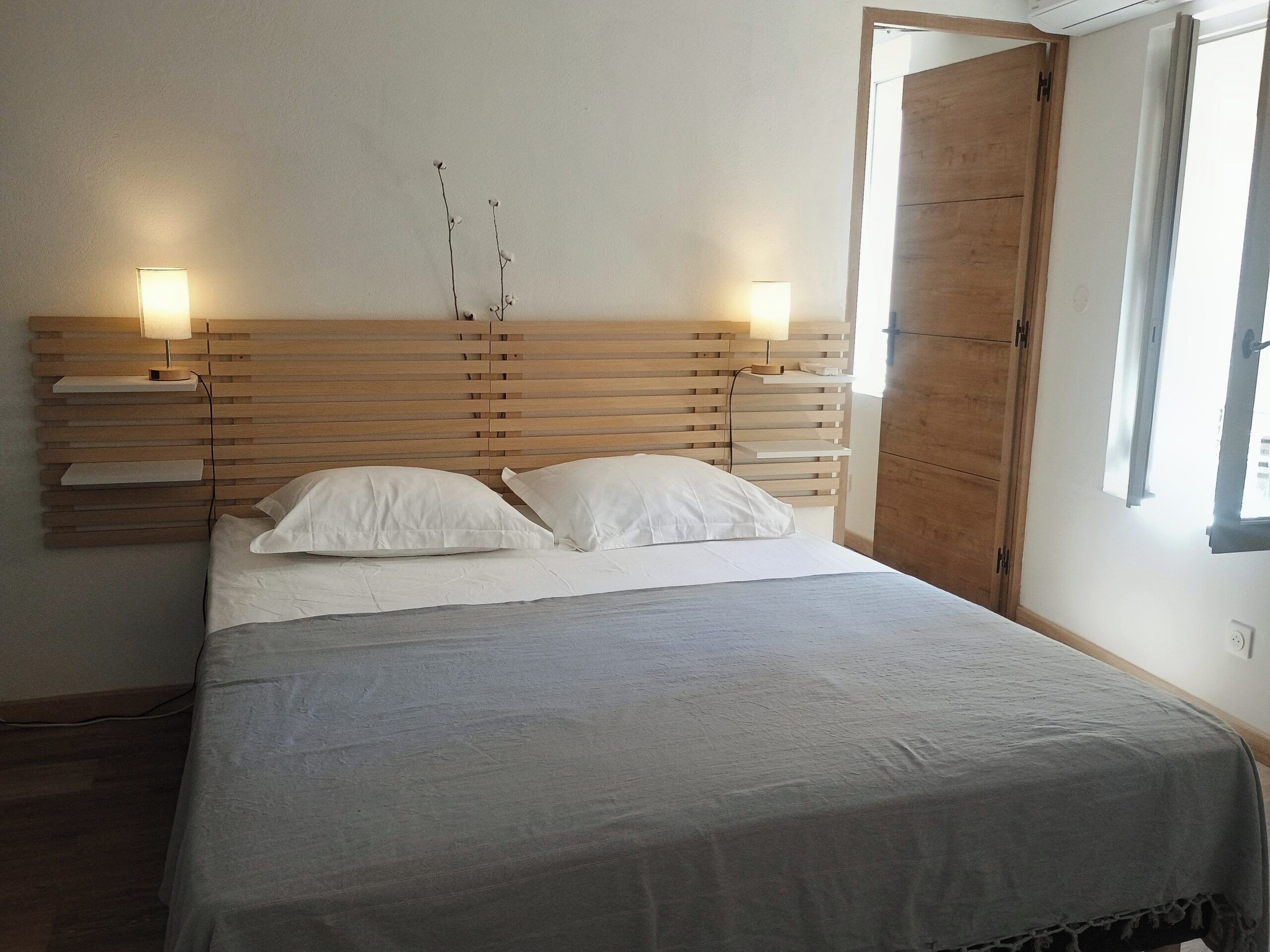 Une chambre à coucher avec une tête de lit en bois, deux tables de chevet avec des lampes, un lit avec une literie blanche et une fenêtre avec des rideaux.