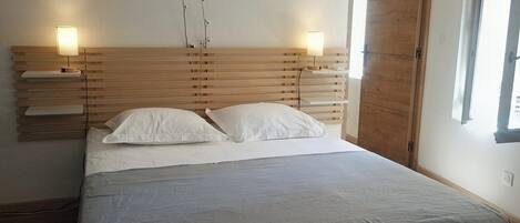 Une chambre à coucher avec une tête de lit en bois, deux tables de chevet avec des lampes, un lit avec une literie blanche et une fenêtre avec des rideaux.