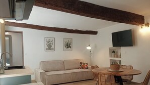 Ein gemütliches Wohnzimmer mit einer Couch, einem Esstisch mit Stühlen, einem Wand-Fernseher und einer Stehlampe.