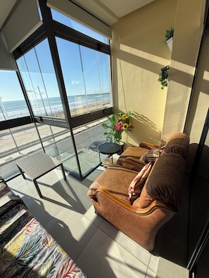 Ein Balkon mit Glastür, einer Couch, einem kleinen Tisch und einem Blumentopf.