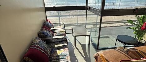 A balcony with a sofa and a table, overlooking a beach.