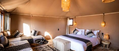 A tented accommodation with a large bed, two smaller beds, and a dining area.