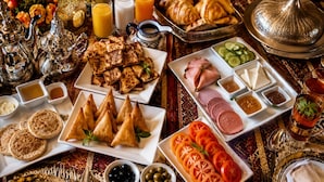 A table set with various dishes, including samosas, bread, and sliced meats, accompanied by condiments and drinks. - Sultan Luxury Camp  (Merzouga)