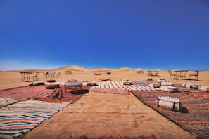Paisaje desértico con zonas de estar al aire libre, mesas y alfombras.