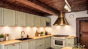 Een keuken met lichtgroene kastjes, een houten aanrecht, een roestvrijstalen afzuigkap, een magnetron en een oven.