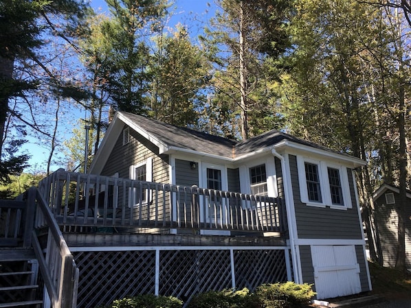 Une cabane à deux étages avec une terrasse, entourée d’arbres.