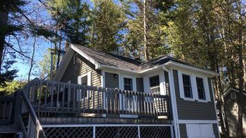 A two-story cabin with a deck, surrounded by trees.