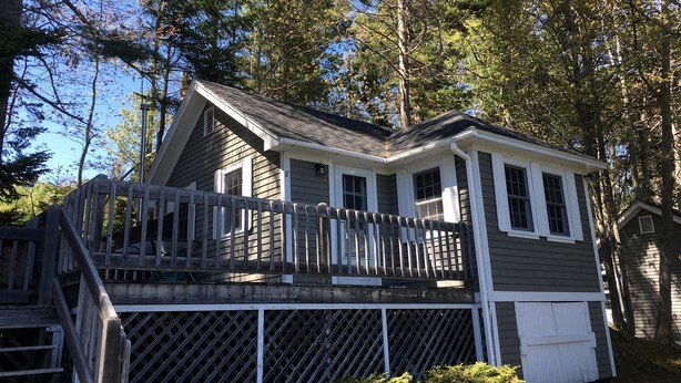 Une cabane à deux étages avec une terrasse, entourée d’arbres.