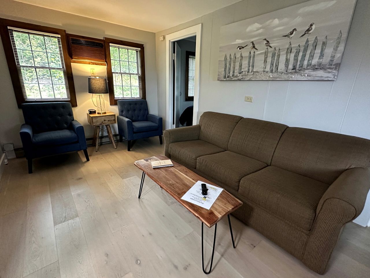 A living room with a brown sofa, two blue armchairs, a wooden coffee table, and a lamp.