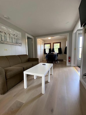 Un salon avec un canapé marron, une table basse blanche et un coin repas comprenant une table et des chaises.
