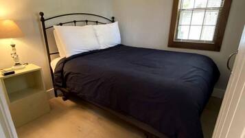 Une petite chambre avec un lit simple, un plancher en bois, une table de chevet avec une lampe et une fenêtre avec des stores.