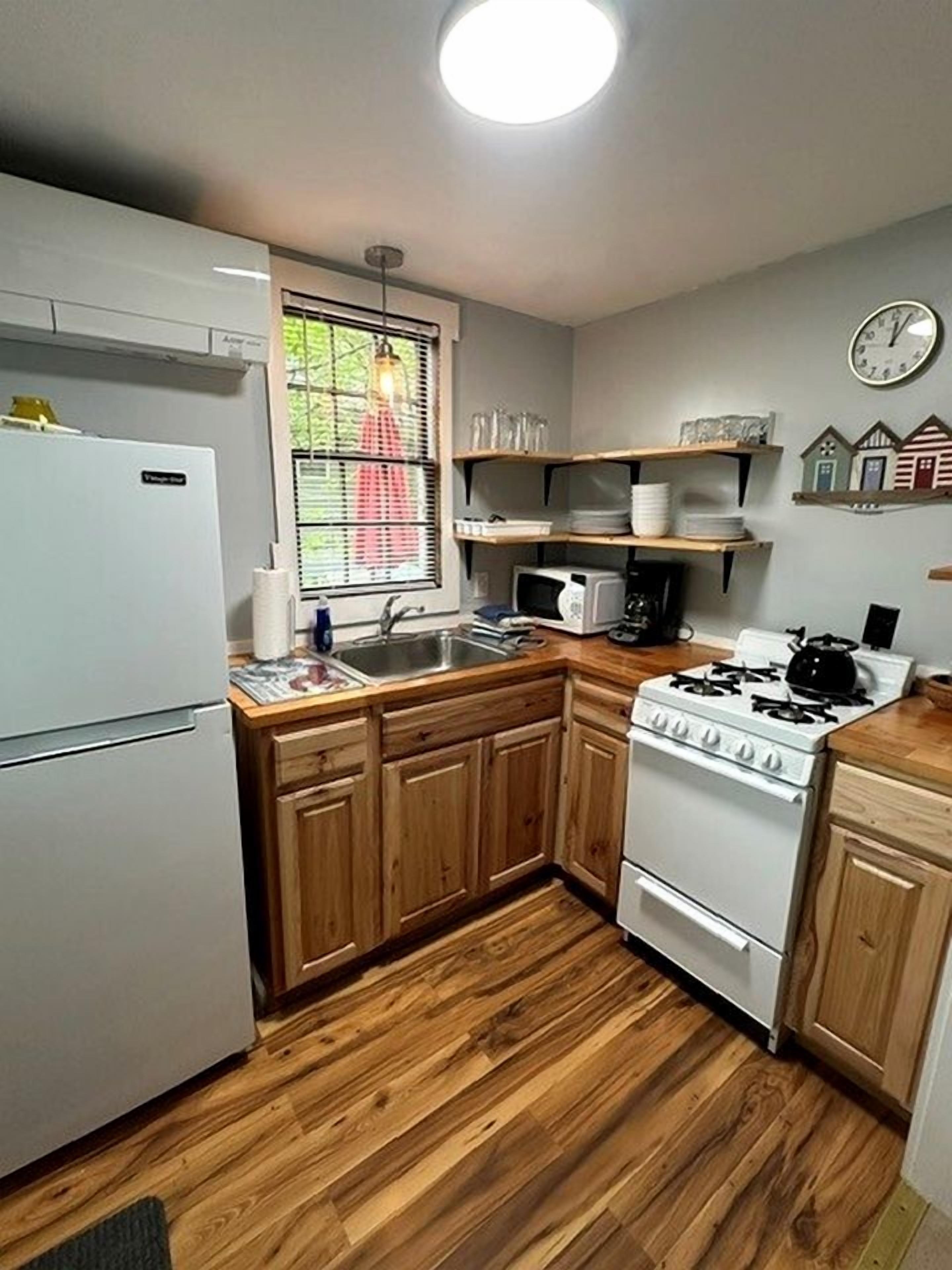 A compact kitchen with wooden cabinets, a white refrigerator, a stove, and a microwave.