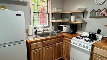 A compact kitchen with wooden cabinets, a white refrigerator, a stove, and a microwave.