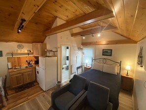 A cozy cabin with a kitchen, a dining area, and a bedroom with a bed and two chairs. - Cozy Cottage with Private Patio & Modern Amenities near Camden, Maine (Lincolnville)